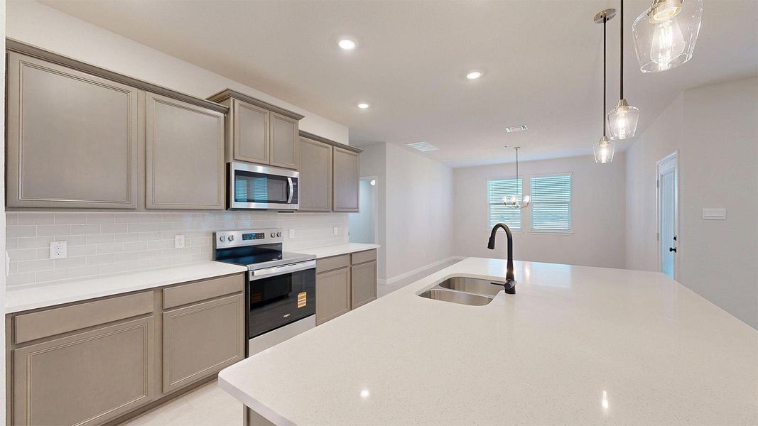 Kitchen featuring stainless steel appliances, tasteful backsplash, a center island with sink, light stone counters, and hanging lights