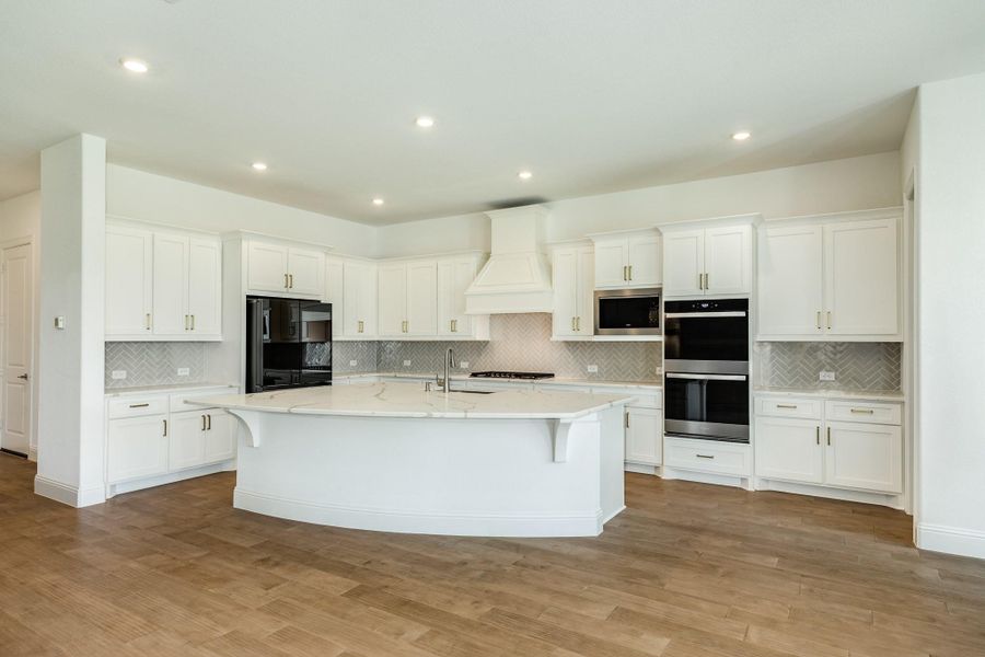 A chef's dream kitchen featuring an oversized granite island with ample seating for five barstools, extensive custom cabinetry, a high-end double oven, and a professional-grade 5-burner range top.