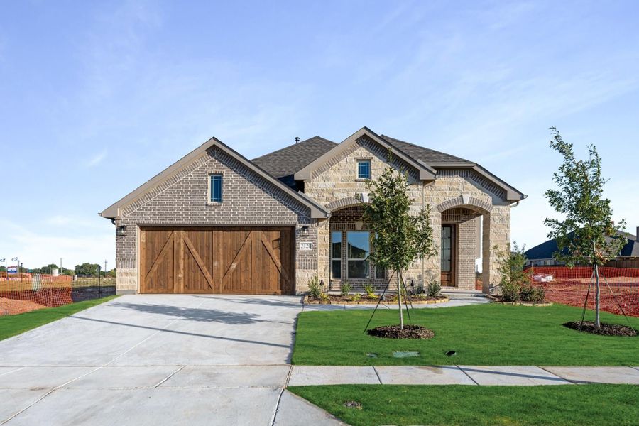 Single-story home with brick and stone exterior, wood garage doors, arched entry, and green front lawn Single-story home with brick and stone exterior, wood garage doors, arched entry, and green front lawn