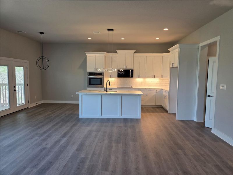 Kitchen featuring white cabinets, oven, an island with sink, decorative light fixtures, and tasteful backsplash Kitchen featuring white cabinets, oven, an island with sink, decorative light fixtures, and tasteful backsplash