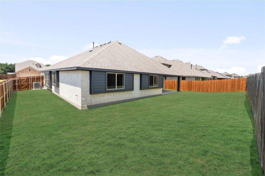 Rear exterior of single-story brick home with gray siding, large fenced backyard, and covered patio Rear exterior of single-story brick home with gray siding, large fenced backyard, and covered patio