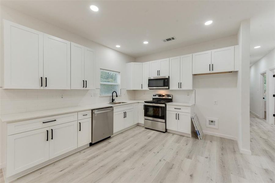 Kitchen with tasteful backsplash, light hardwood / wood-style flooring, sink, appliances with stainless steel finishes, and white cabinets