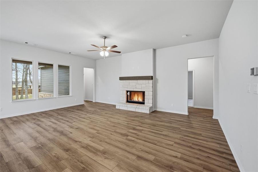 Unfurnished living room with a ceiling fan, a stone fireplace, and wood finished floors Unfurnished living room with a ceiling fan, a stone fireplace, and wood finished floors