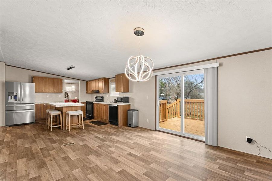 Kitchen with light countertops, black appliances, wood finish cabinetry, suspended lighting, and light wood-type flooring