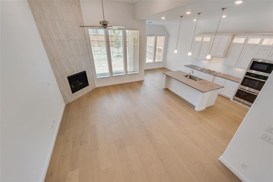 Kitchen with white cabinetry, tasteful backsplash, a center island with sink, light hardwood / wood-style flooring, and a tiled fireplace