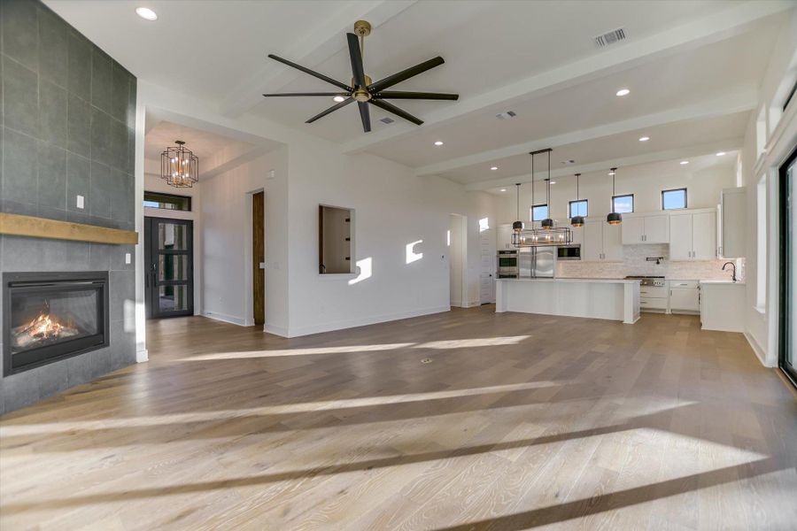 Living room featuring a ceiling fan, a fireplace, light wood-style floors, beam ceiling, and suspended lighting