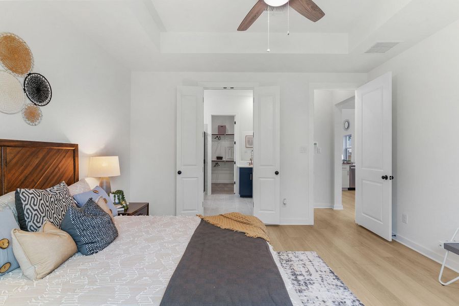 Bedroom with a tray ceiling, light wood finished floors, baseboards, ensuite bathroom, and ceiling fan