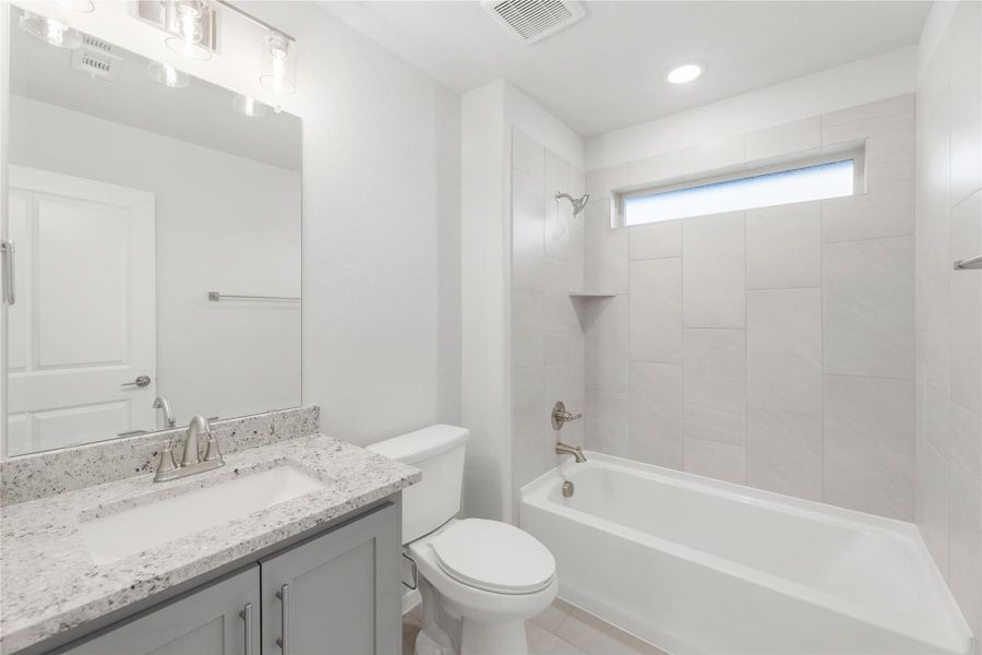Bathroom with granite countertop vanity, white tub-shower combo with tile surround, and small window
