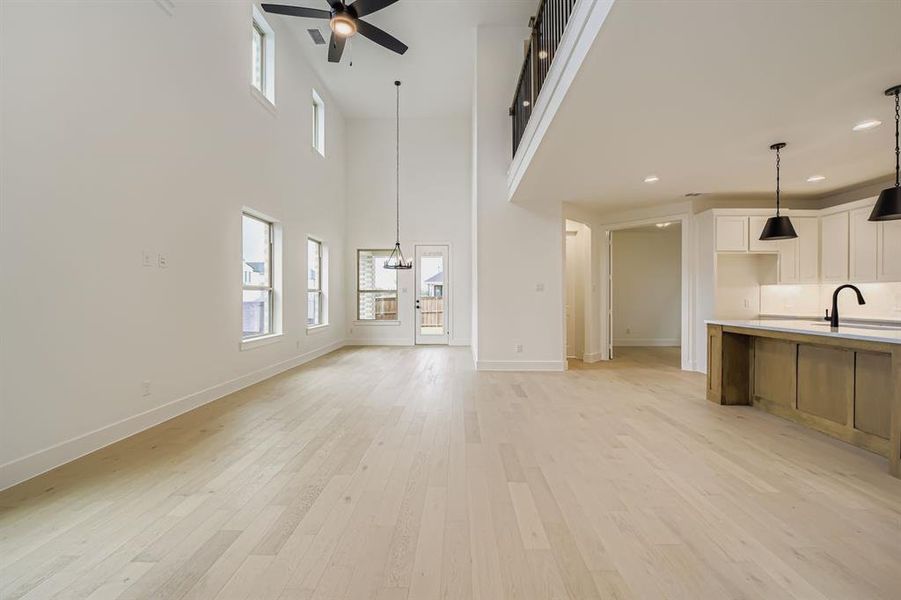Unfurnished living room featuring light wood-style flooring, plenty of natural light, a ceiling fan, a towering ceiling, and a chandelier Unfurnished living room featuring light wood-style flooring, plenty of natural light, a ceiling fan, a towering ceiling, and a chandelier