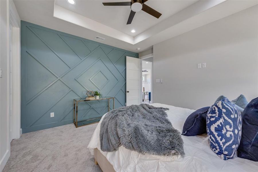 Carpeted bedroom featuring a raised ceiling and ceiling fan