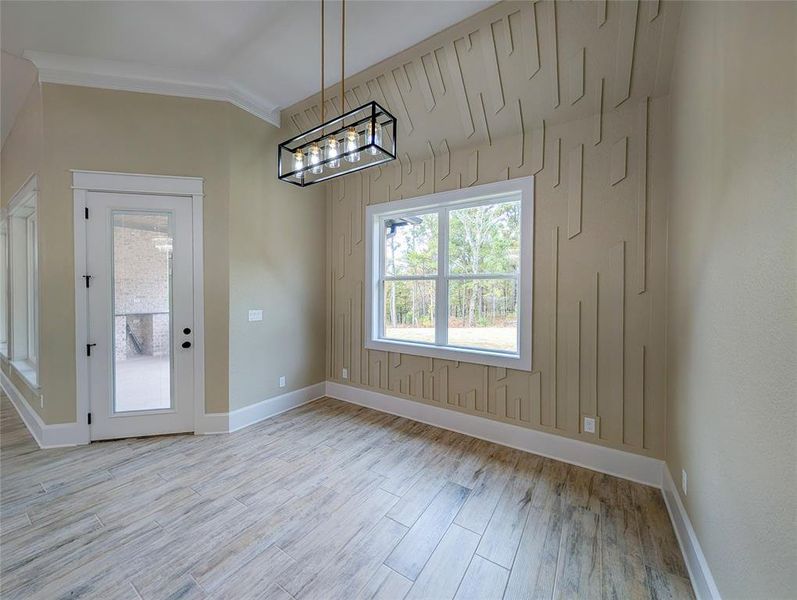 Unfurnished dining area featuring light wood finished floors, a chandelier, and crown molding