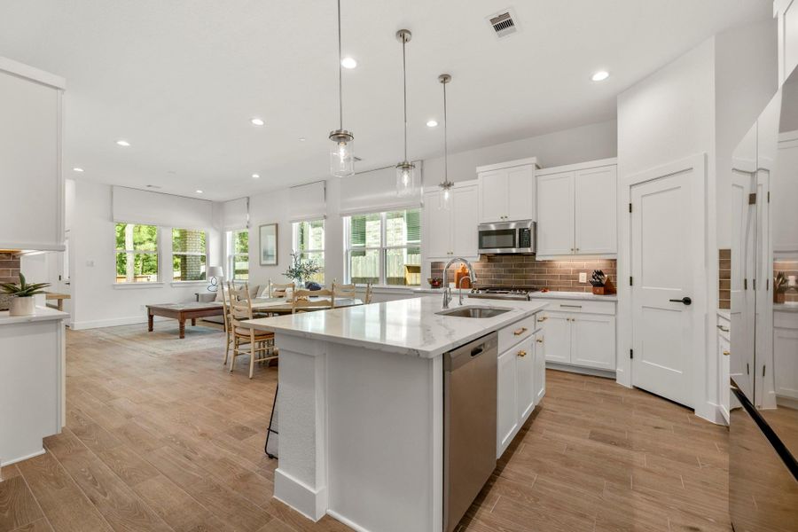 Enjoy a bright, open-concept kitchen and dining space. It features modern white cabinetry, a large island with a sink, stainless steel appliances, and pendant lighting. The space is complemented by wood-look tile flooring and large windows that provide plenty of natural light. Enjoy a bright, open-concept kitchen and dining space. It features modern white cabinetry, a large island with a sink, stainless steel appliances, and pendant lighting. The space is complemented by wood-look tile flooring and large windows that provide plenty of natural light.