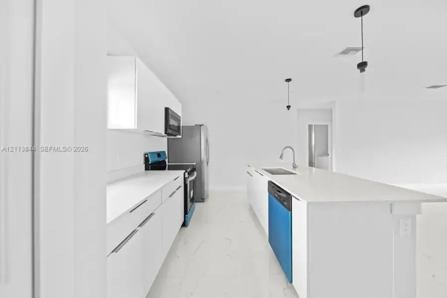 Kitchen featuring white flat-panel cabinetry, stone-finish countertops, central island with integrated stainless steel sink, large-format tile flooring, and pendant lighting Kitchen featuring white flat-panel cabinetry, stone-finish countertops, central island with integrated stainless steel sink, large-format tile flooring, and pendant lighting