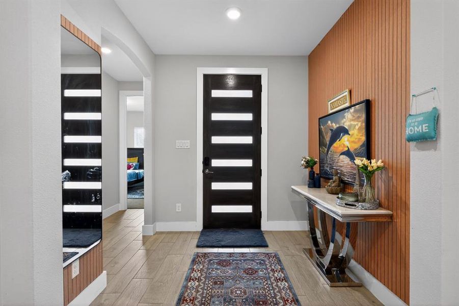 Inviting entryway featuring light wood-look flooring, a modern front door with frosted glass inserts, and an accent wall with vertical wood paneling
