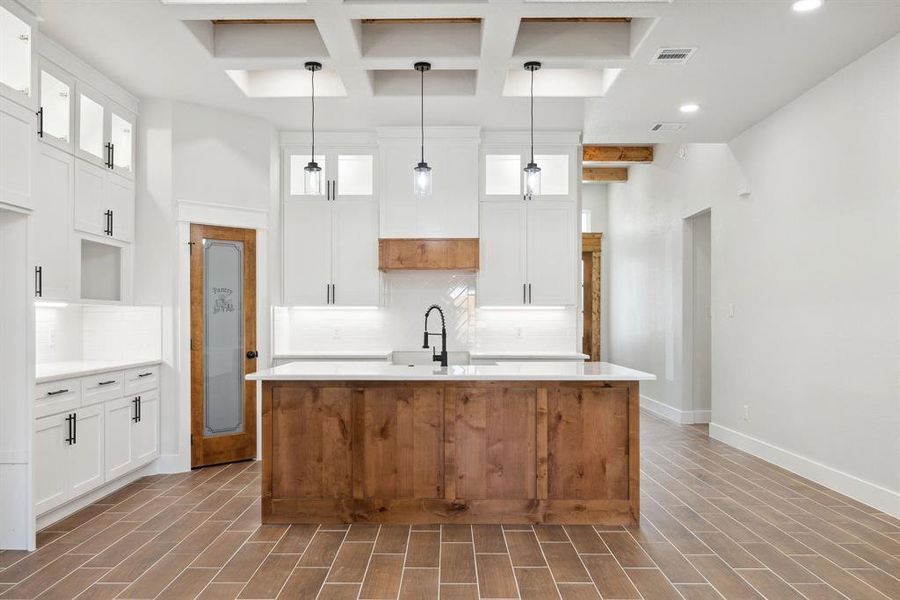 Kitchen with pendant lighting, a kitchen island with sink, and white cabinets