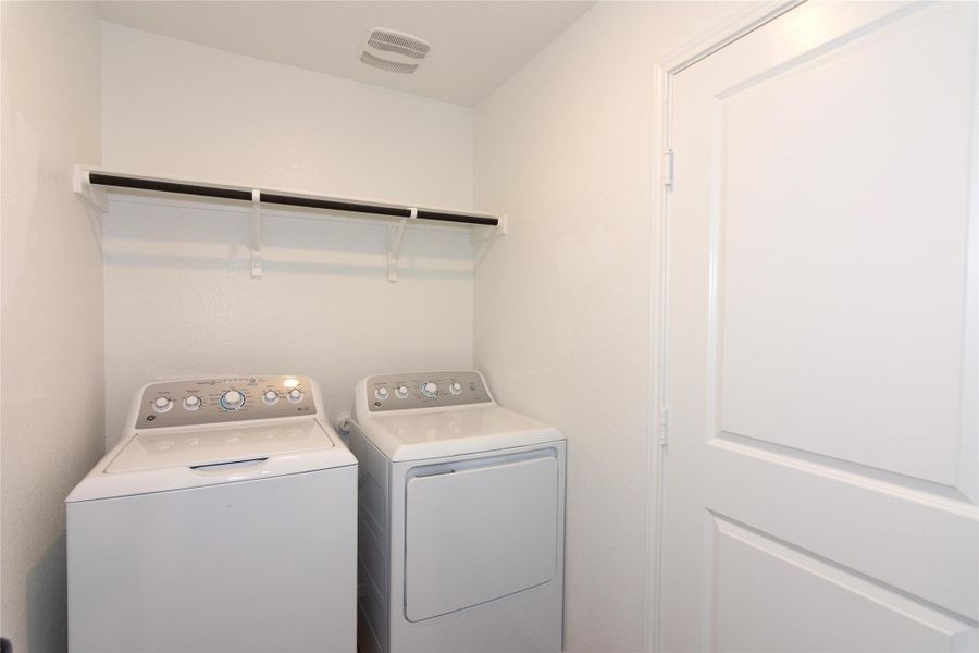 Dedicated laundry area with a built-in hanging rod, wall shelving, white walls, and a white paneled door