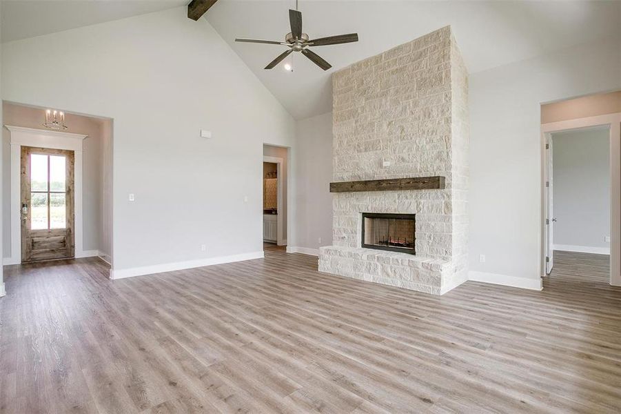 Unfurnished living room with ceiling fan with notable chandelier, hardwood / wood-style flooring, a stone fireplace, beam ceiling, and high vaulted ceiling