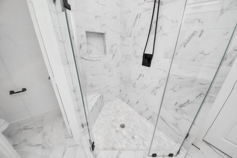 This is a modern shower with sleek glass doors and elegant marble-style tiles, featuring a built-in shower bench and a convenient wall niche for storage. This is a modern shower with sleek glass doors and elegant marble-style tiles, featuring a built-in shower bench and a convenient wall niche for storage.
