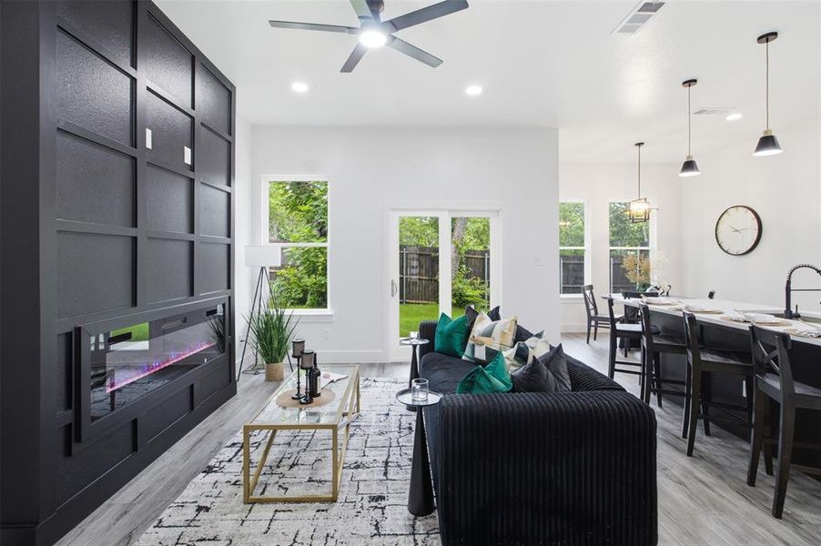 Open-concept living area featuring an electric fireplace within a paneled feature wall, wood-finish flooring, recessed lighting, and a modern ceiling fan