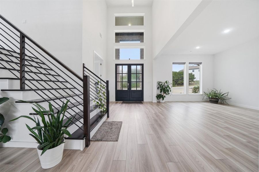 Inviting entryway featuring light wood flooring, a striking black metal staircase, a dark paneled front door, and high ceilings with transom windows