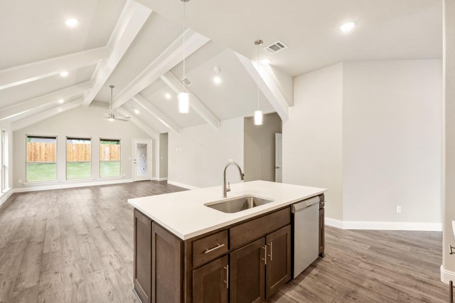 Kitchen island with sink and dark cabinets, open to living area with vaulted beam ceiling and wood floors