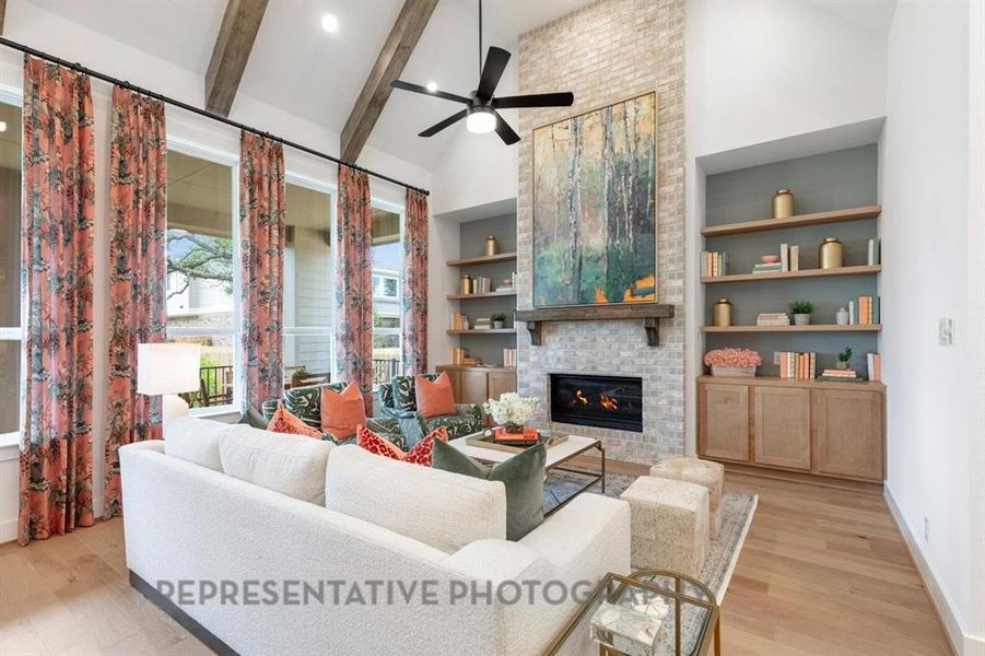 Living area featuring built in features, a fireplace, light wood-style floors, beam ceiling, and high vaulted ceiling