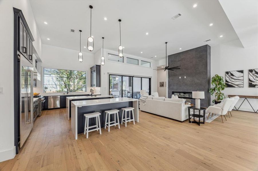 This kitchen features an open-concept layout with a large central island, high ceilings, and pendant lighting, seamlessly flowing into the adjacent family room for a cohesive and spacious design.