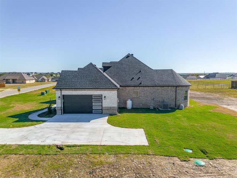 View of property exterior with concrete driveway, brick siding, roof with shingles, and a garage