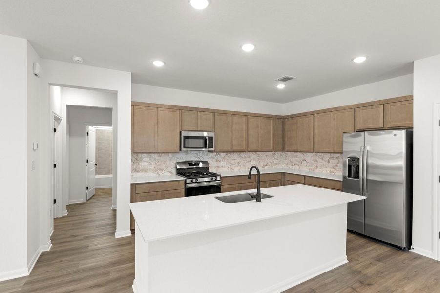 Kitchen featuring appliances with stainless steel finishes, a center island with sink, dark wood finished floors, light stone counters, and backsplash