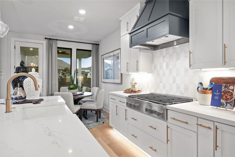 Kitchen featuring white cabinets, premium range hood, backsplash, light wood-style flooring, and stainless steel gas cooktop