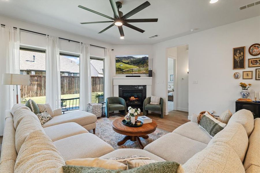 Living room featuring wood finished floors, recessed lighting, a glass covered fireplace, and an oversized ceiling fan Living room featuring wood finished floors, recessed lighting, a glass covered fireplace, and an oversized ceiling fan