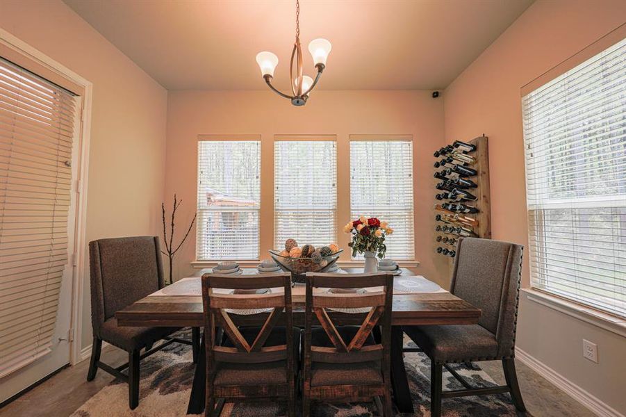 This photo showcases a cozy dining area with a wooden table set for four. It features large windows that provide plenty of natural light and a wall-mounted wine rack for added charm. The neutral walls and simple chandelier create a warm, inviting atmosphere.