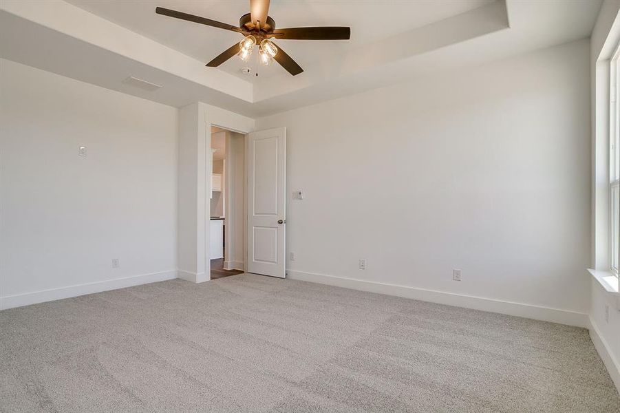 Unfurnished room with a tray ceiling, light colored carpet, and ceiling fan Unfurnished room with a tray ceiling, light colored carpet, and ceiling fan