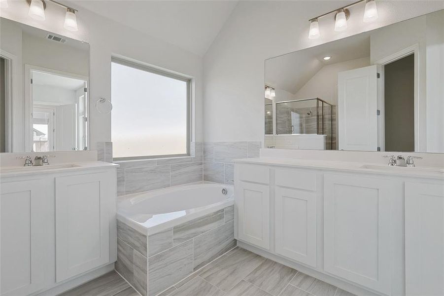Bathroom featuring two vanities, a shower stall, lofted ceiling, and a garden tub