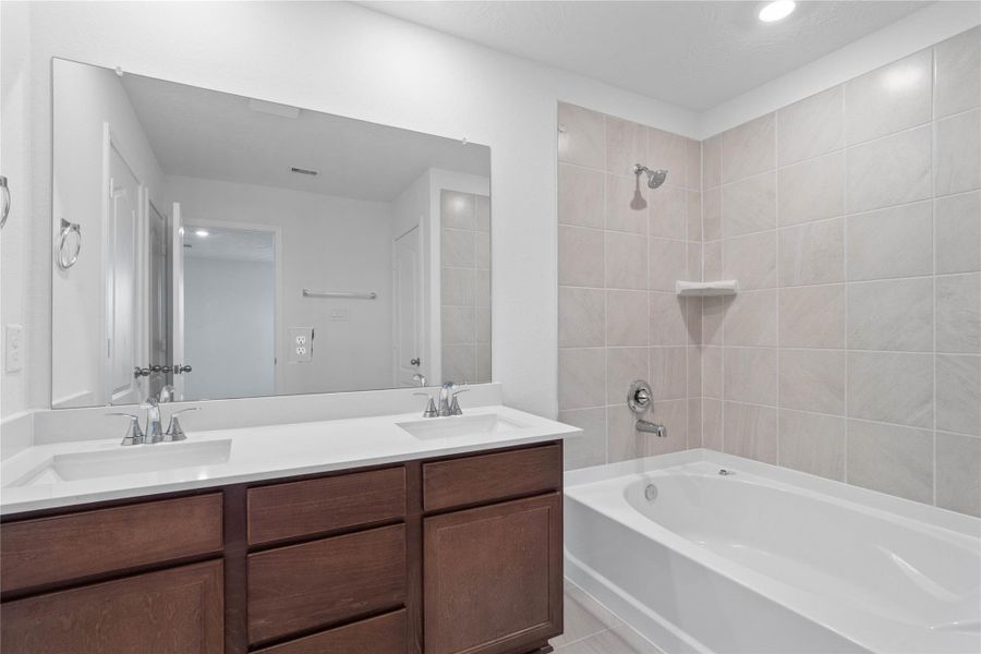 This beautiful primary bathroom is move-in ready! It showcases stained cabinetry paired with light countertops, dual vanity sinks, a large mirror, high ceilings, custom paint, tub/shower combination, and stylish modern finishes throughout.
