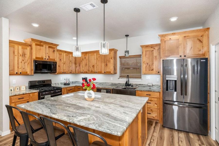 Kitchen featuring light stone counters, a center island, hanging light fixtures, light wood-type flooring, and stainless steel appliances