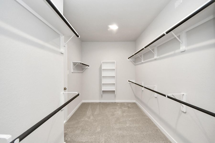 Experience luxury in this spacious walk-in closet with high ceilings and plush carpet. Warm paint tones, built-in shelving, and dark finishes create a contemporary and functional retreat. Sample photo of completed home with similar floor plan. Actual colors and selections may vary. Experience luxury in this spacious walk-in closet with high ceilings and plush carpet. Warm paint tones, built-in shelving, and dark finishes create a contemporary and functional retreat. Sample photo of completed home with similar floor plan. Actual colors and selections may vary.