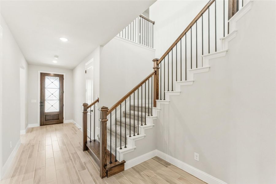 Entryway with wood staircase, metal balusters, light hardwood floors, and glass-panel front door Entryway with wood staircase, metal balusters, light hardwood floors, and glass-panel front door