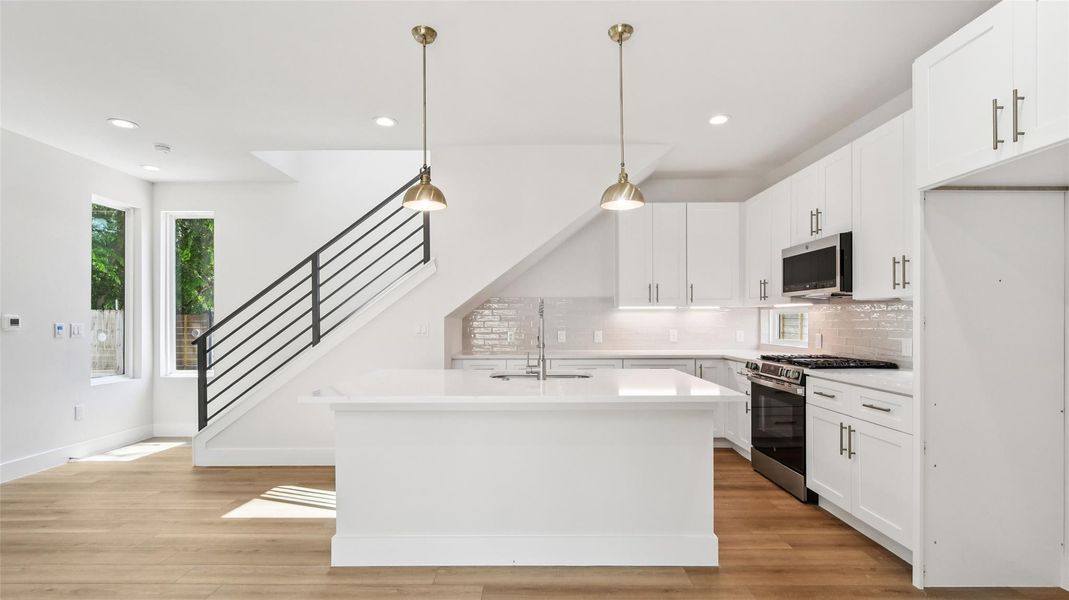 Kitchen featuring white cabinetry, stainless steel appliances, pendant lighting, recessed lighting, and light wood finished floors Kitchen featuring white cabinetry, stainless steel appliances, pendant lighting, recessed lighting, and light wood finished floors