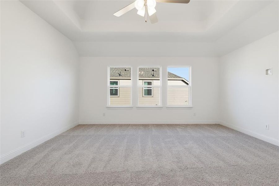 Empty room with light colored carpet, ceiling fan, and a raised ceiling Empty room with light colored carpet, ceiling fan, and a raised ceiling