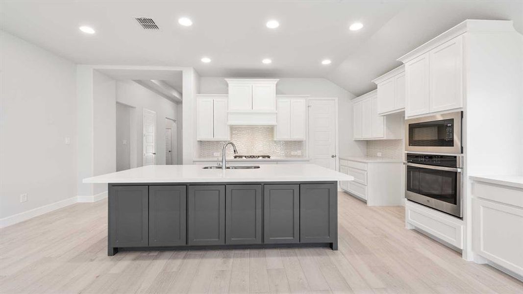 Kitchen with a center island with sink, stainless steel oven, lofted ceiling, black microwave, and white cabinets