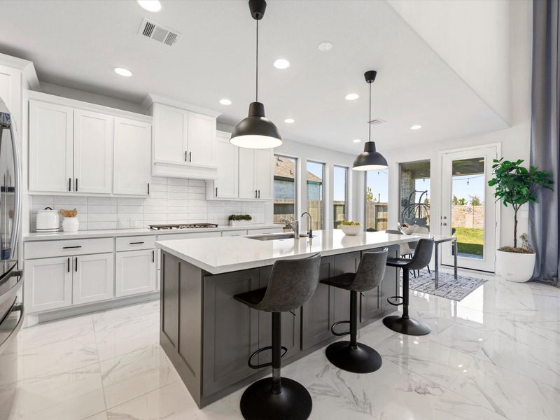 Bright, open-concept kitchen with a large center island, sleek quartz countertops, and contrasting cabinetry. Features stainless steel appliances, modern pendant lighting, and expansive windows that bring in natural light and views of the backyard—ideal for both everyday living and entertaining.
