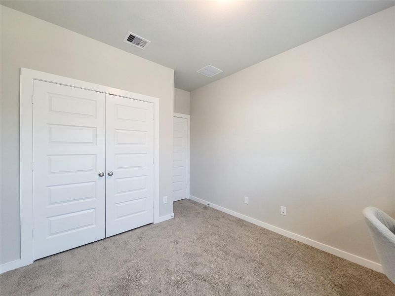 This is a bright, neutral-color secondary bedroom with carpeted flooring and a double-door closet. It's ideal for a bedroom or home office.