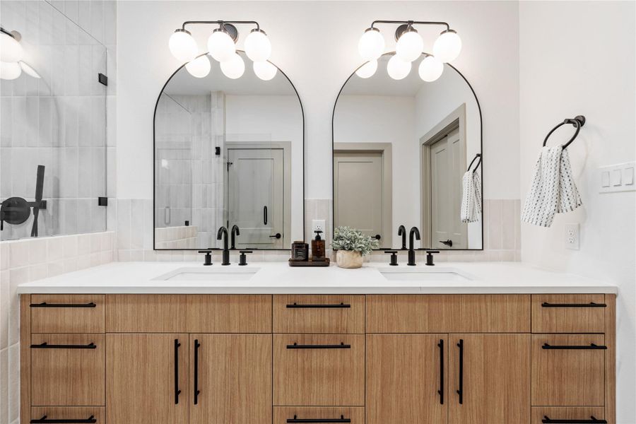This spa-like primary bathroom blends contemporary luxury with timeless design—featuring a floating dual vanity with quartz counters, arched mirrors, matte black fixtures, and a frameless glass shower. A soaking tub tucked beneath a picture window completes the retreat, offering a perfect place to unwind in style.