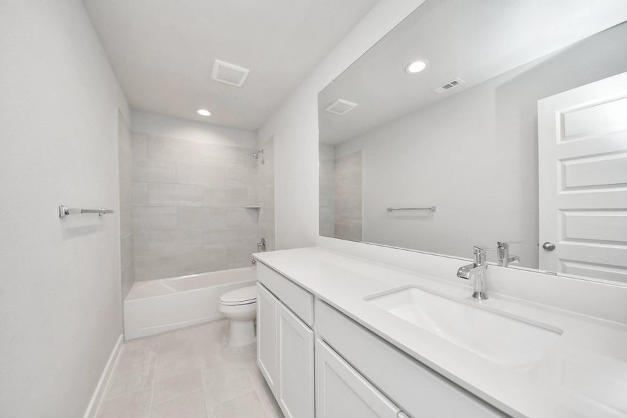 Secondary bath features tile flooring, bath/shower combo with tile surround, light stained wood cabinets, beautiful light countertop.