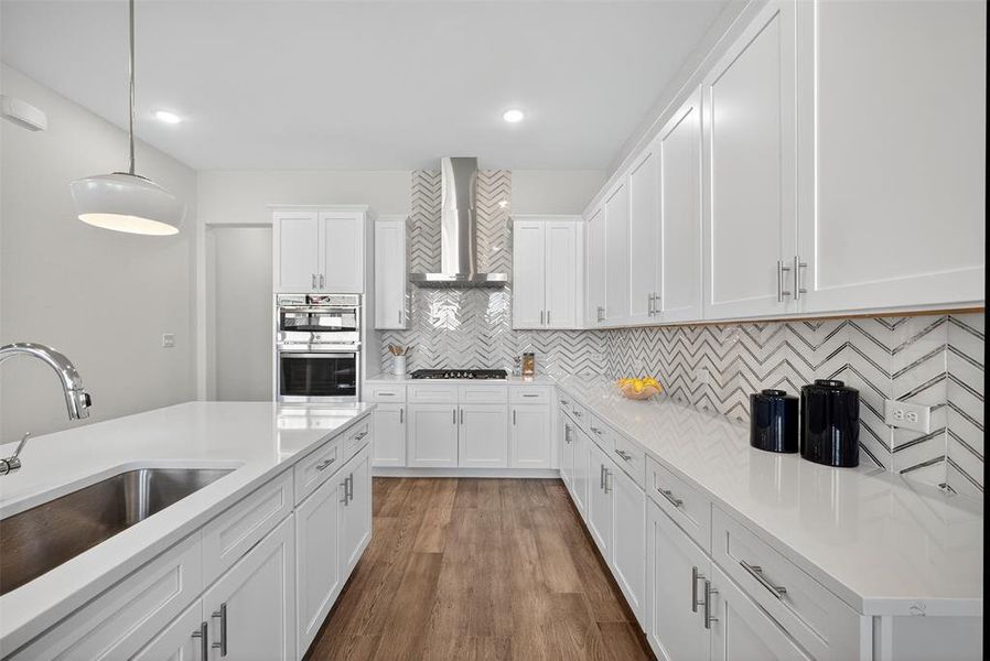 Kitchen with decorative light fixtures, tasteful backsplash, white cabinets, dark wood-style floors, and wall chimney range hood Kitchen with decorative light fixtures, tasteful backsplash, white cabinets, dark wood-style floors, and wall chimney range hood