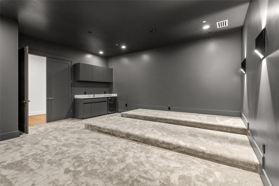 Movie night at its finest—this tiered-floor media room is built for comfort, with plenty of room for oversized seating, ambient wall-mounted lighting, and charcoal gray walls for a true theater feel. With no windows and a built-in bar featuring a quartzite countertop, storage, and beverage fridge, it’s designed for the ultimate at-home viewing experience. Movie night at its finest—this tiered-floor media room is built for comfort, with plenty of room for oversized seating, ambient wall-mounted lighting, and charcoal gray walls for a true theater feel. With no windows and a built-in bar featuring a quartzite countertop, storage, and beverage fridge, it’s designed for the ultimate at-home viewing experience.