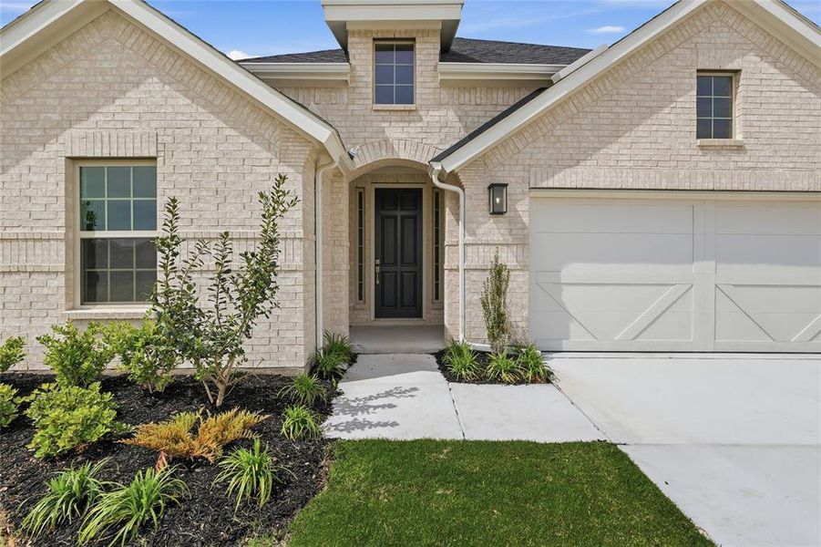 Property entrance featuring roof with shingles, an attached garage, concrete driveway, and brick siding