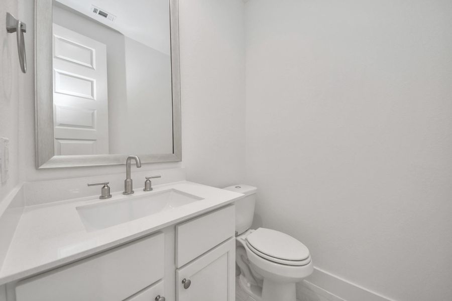 Sophisticated half bathroom adorned with contemporary finishes. The elegant 5-panel door welcomes you to a space where style meets functionality. Notice the sleek hardware accents that add a touch of modern charm. The vanity boasts light-colored countertops, beautifully complemented by a tasteful vanity light, creating a well-lit and inviting atmosphere.