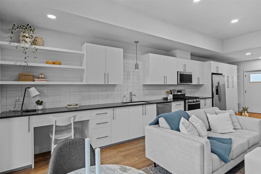 Kitchen featuring stainless steel appliances, dark countertops, backsplash, a sink, and light wood-type flooring